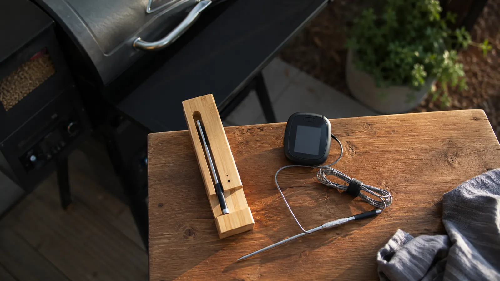Two wireless meat thermometers side by side on a wooden table next to a Pit Boss pellet grill